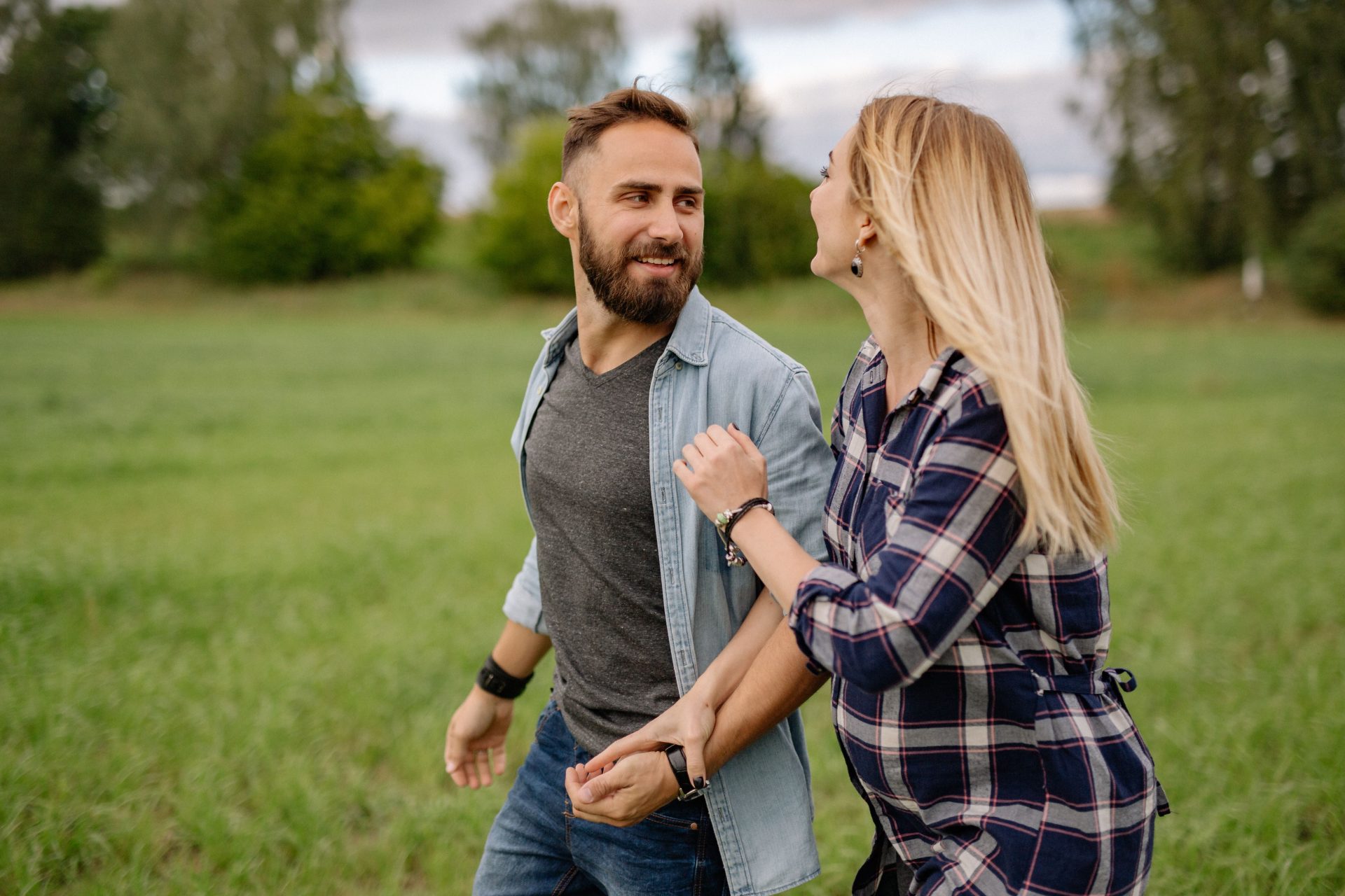 Un couple souriant marche main dans la main à travers un champ verdoyant, partageant un moment de joie.