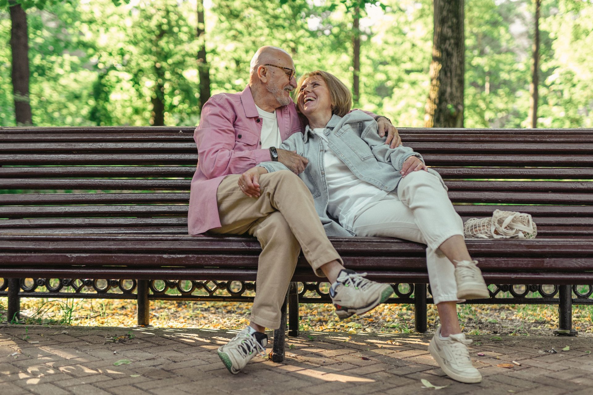 Un couple de personnes âgées profite d'une journée ensoleillée au parc, partageant amour et rires sur un banc.