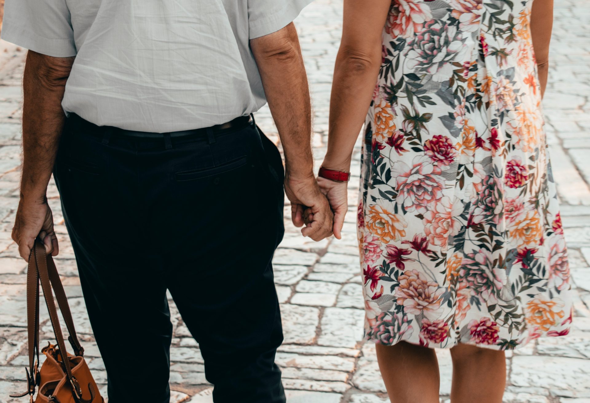Un homme en veste noire et jean bleu se tient à côté d'une femme en manteau beige en plein jour.